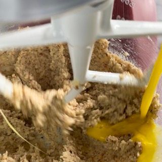 Una persona sta mescolando un impasto in una planetaria con un cucchiaio giallo.