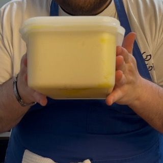 Un uomo con un grembiule tiene in mano un contenitore di burro