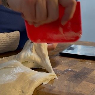 Una persona tiene una spatola rossa sopra un pezzo di pasta