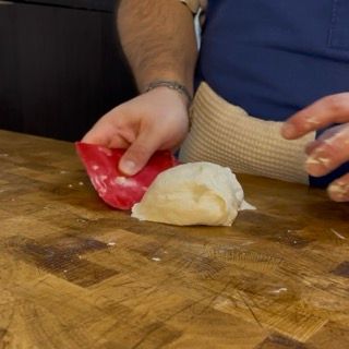 Una persona tiene una spatola rossa sopra un pezzo di pasta su un tagliere