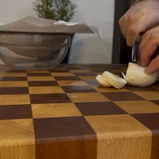 Una persona sta tagliando una cipolla su un tagliere a scacchi