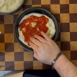 Una persona sta mettendo la salsa di pomodoro su una pizza