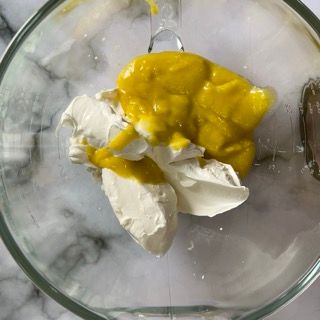 Una ciotola di vetro piena di salsa gialla e panna montata.