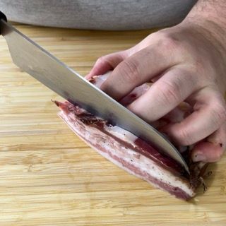 Una persona sta tagliando un pezzo di pancetta su un tagliere