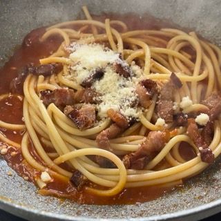 Una padella di spaghetti con carne e formaggio sopra