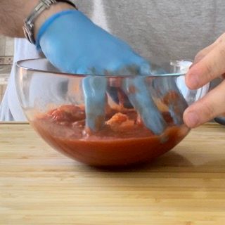 Una persona che indossa guanti blu sta mescolando una ciotola di salsa di pomodoro.