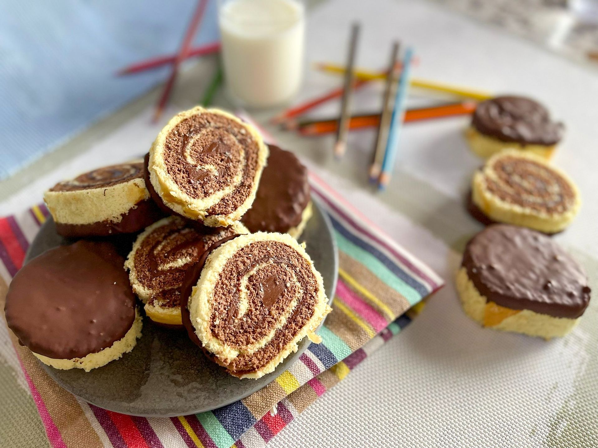Un piatto di biscotti ricoperti di cioccolato su un tavolo accanto a un bicchiere di latte.