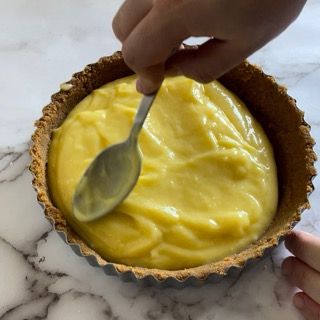 Una persona tiene in mano un cucchiaio in una ciotola di liquido giallo