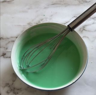 Una ciotola di liquido verde con una frusta dentro