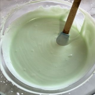 Un cucchiaio di legno è in una ciotola di liquido verde.