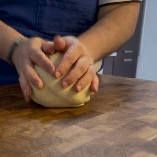 Una persona tiene in mano una palla di pasta su un tagliere