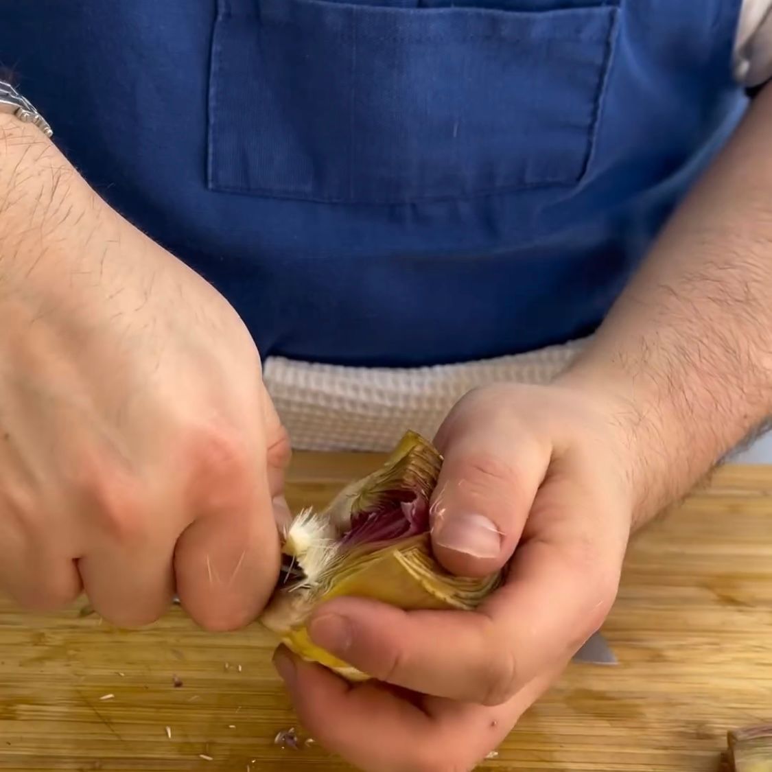 Un uomo con un grembiule blu sta sbucciando un carciofo