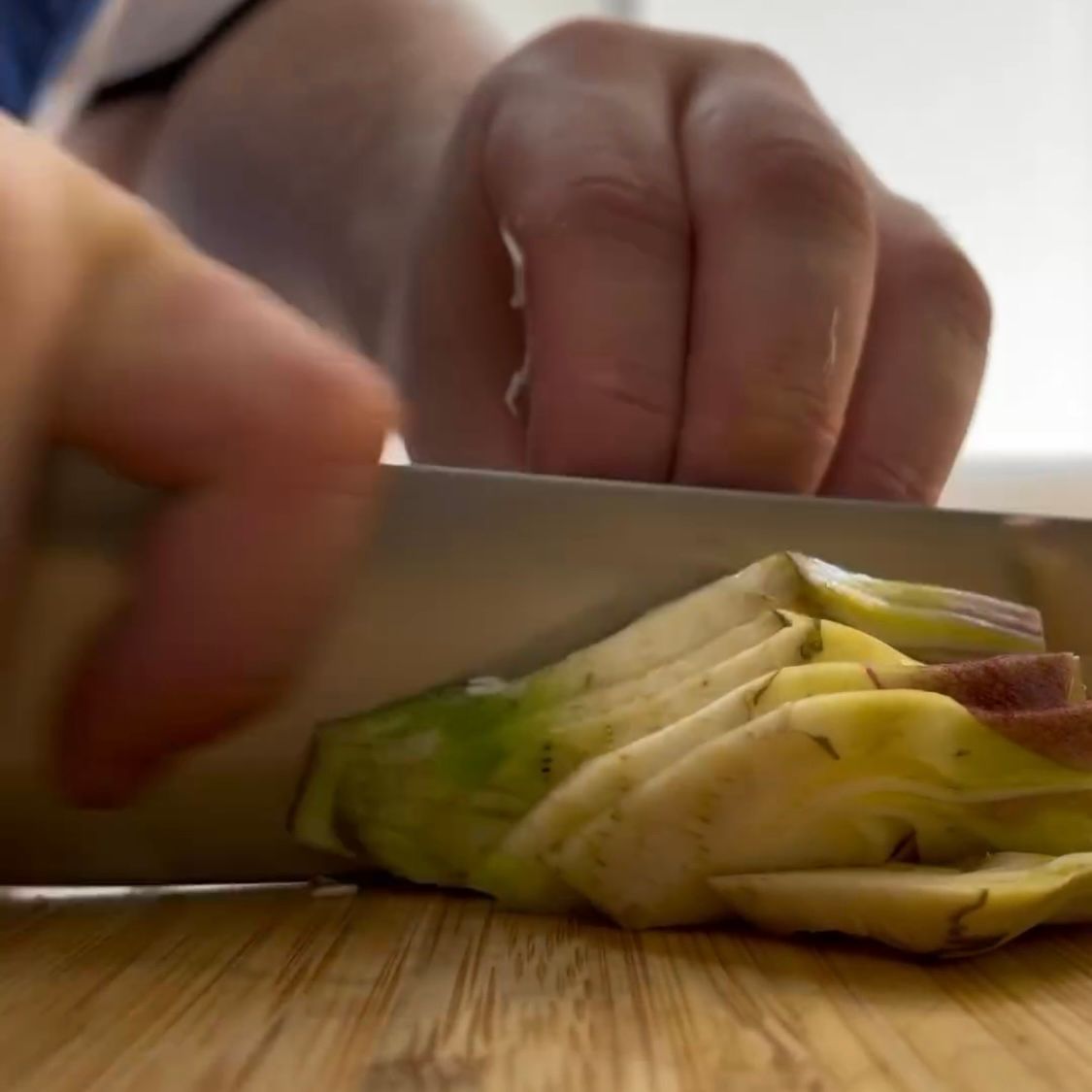 Una persona sta tagliando i carciofi su un tagliere di legno