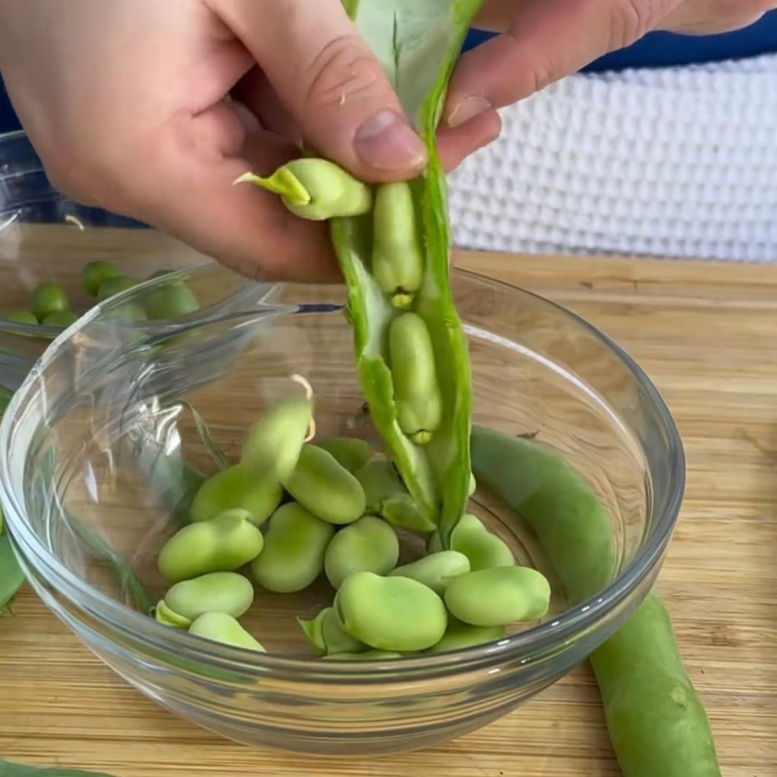 Una persona sta sbucciando i fagiolini in una ciotola di vetro.