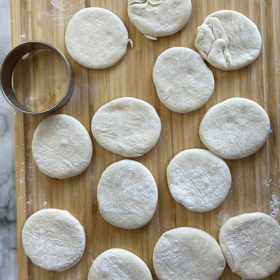 Un tagliere di legno sul quale sono sistemate delle palline di pasta e un tagliabiscotti.