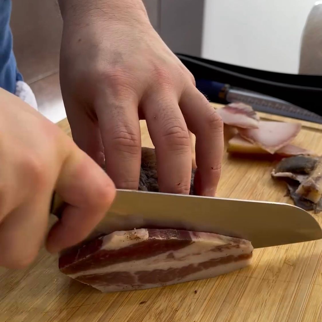 Una persona sta tagliando un pezzo di pancetta su un tagliere