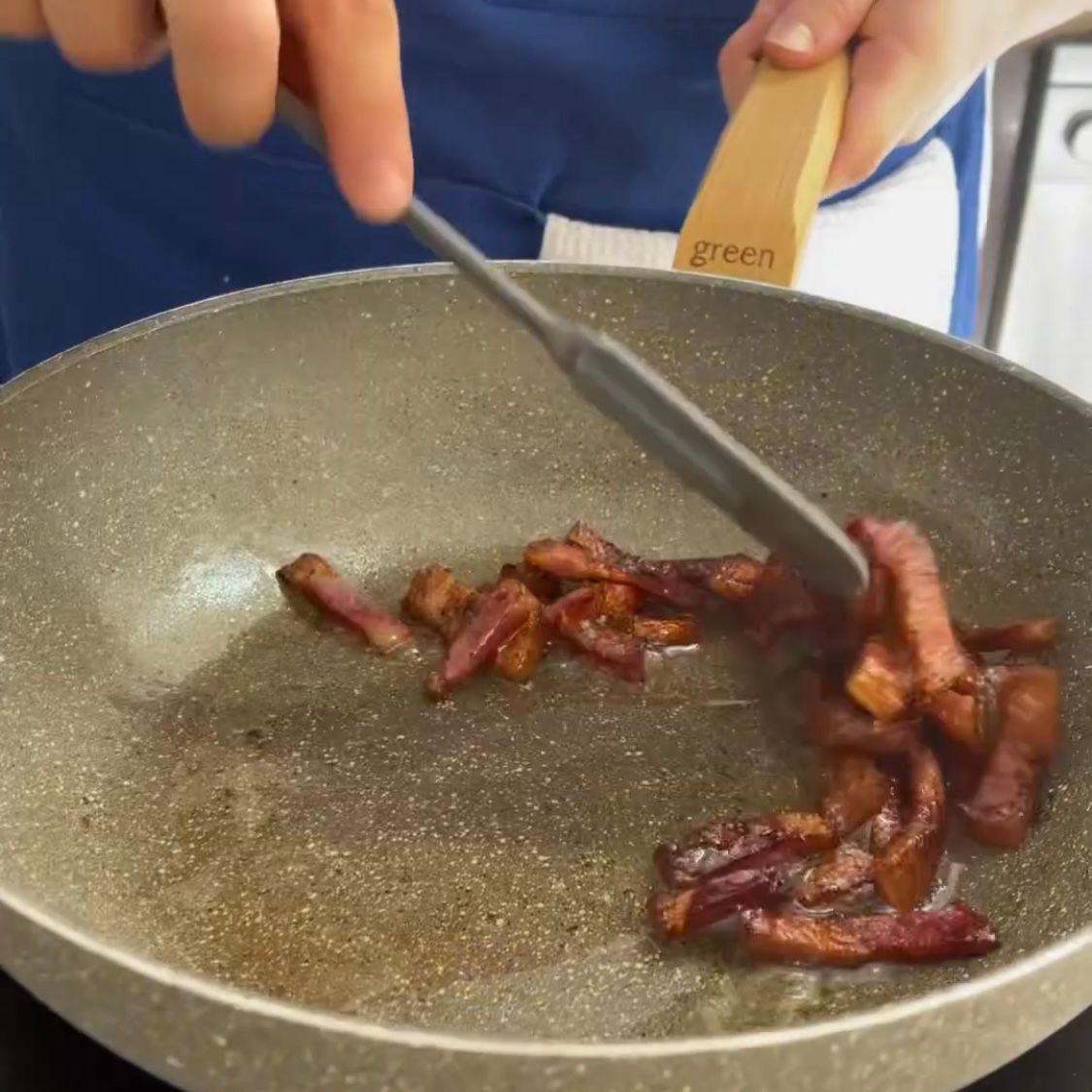 Una persona sta mescolando la pancetta in una padella con una spatola verde