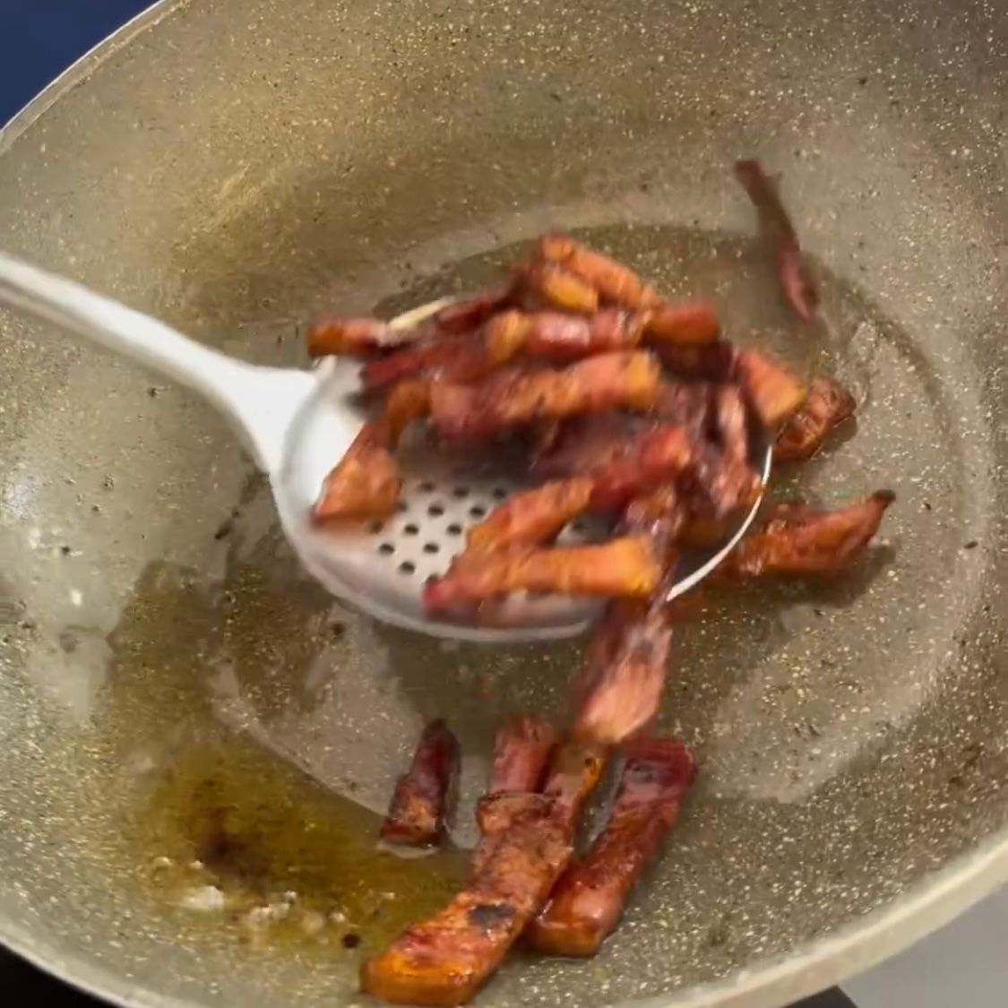 Una padella piena di pancetta e un cucchiaio dentro.