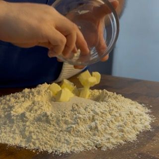 Una persona sta versando il burro in un mucchio di farina