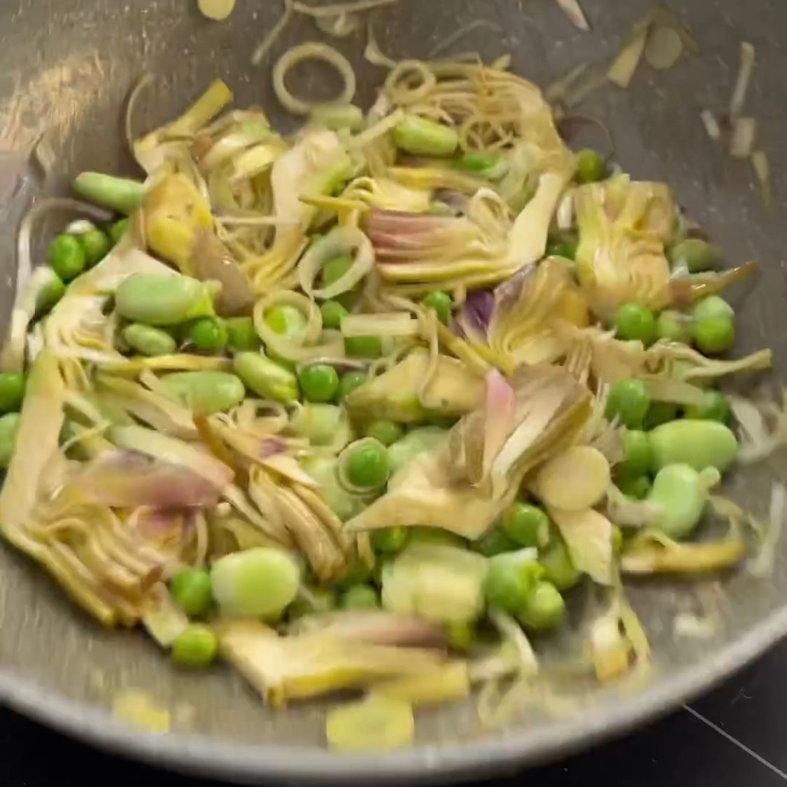 Una padella piena di carciofi, piselli, cipolle e altre verdure.