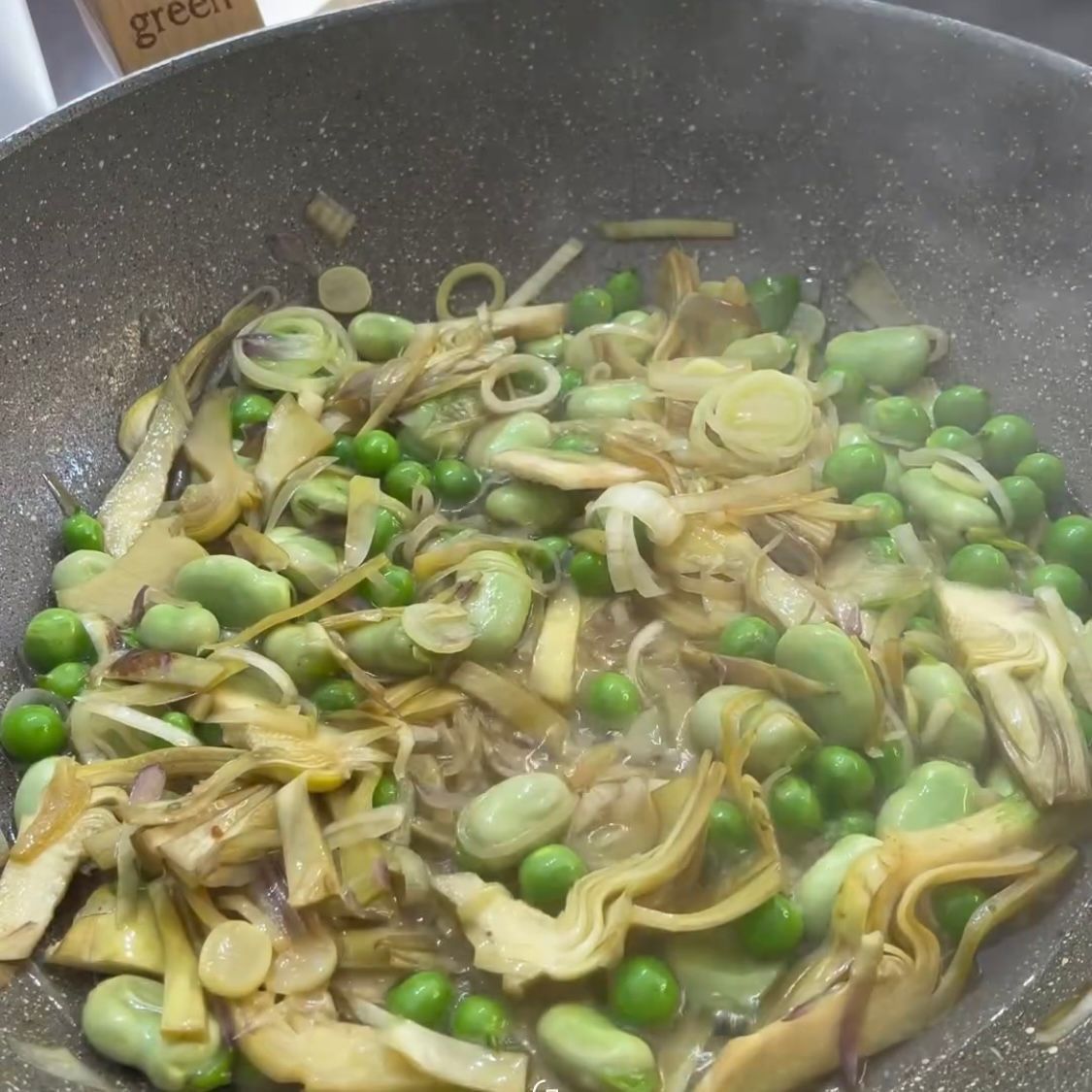 Una padella piena di verdure tra cui piselli e carciofi