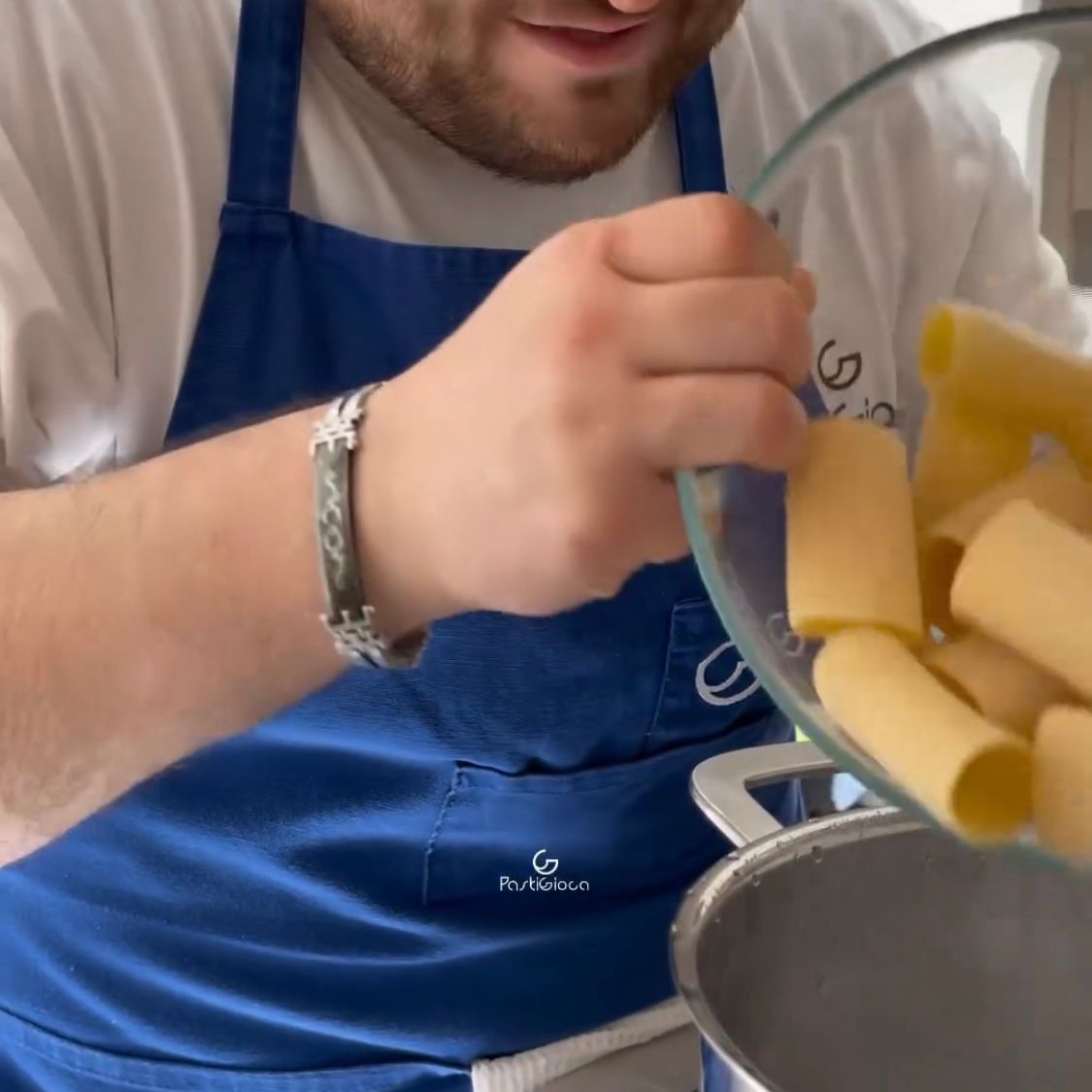 Un uomo con un grembiule blu sta versando la pasta in una pentola