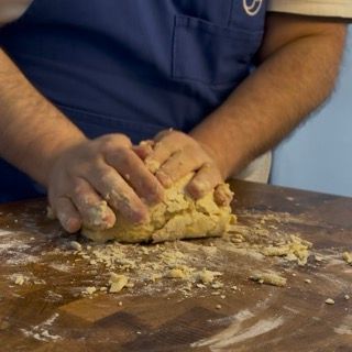 Una persona con un grembiule blu che impasta la pasta su un tavolo di legno