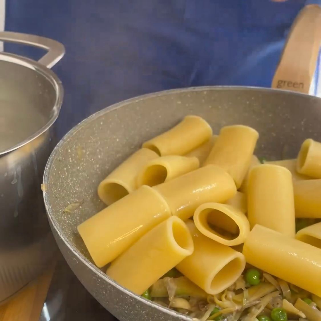 Una padella piena di pasta e piselli accanto a una pentola di acqua bollente