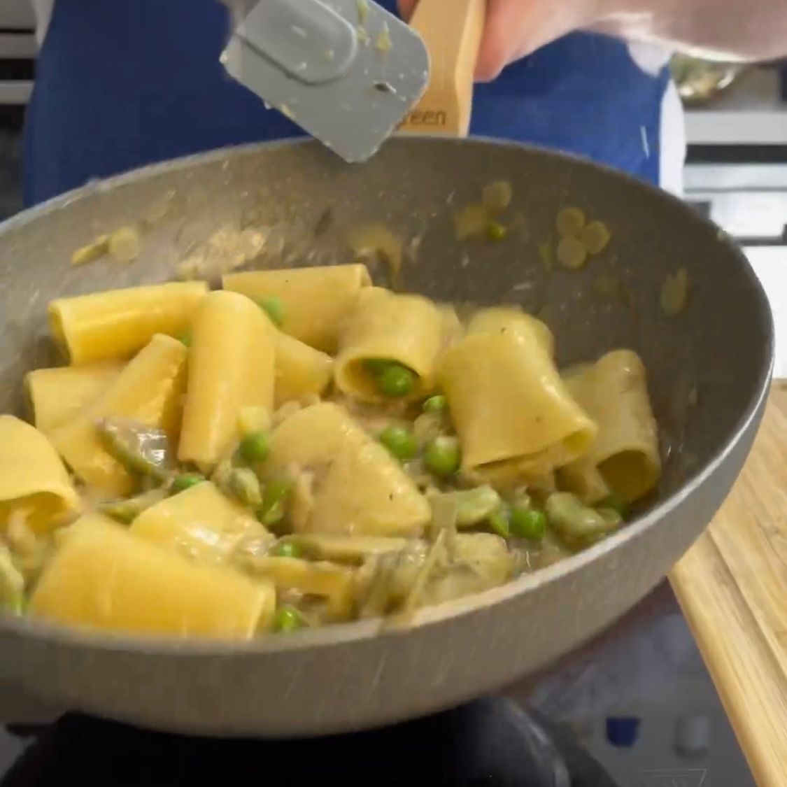 Una persona tiene una spatola sopra una padella di pasta e piselli