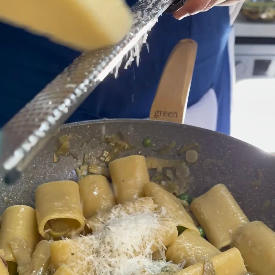 Una persona che grattugia il formaggio sulla pasta in una padella con la scritta verde