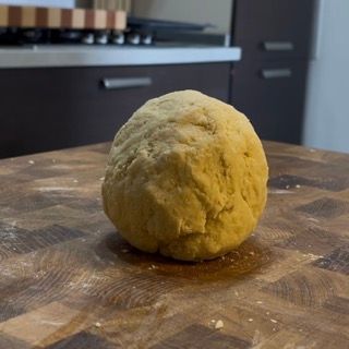 Una palla di pasta è appoggiata su un tagliere di legno