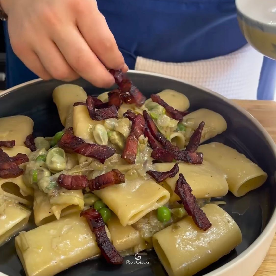 Una persona aggiunge la pancetta a un piatto di pasta