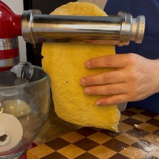 Una persona tiene in mano un pezzo di pasta davanti a un mixer KitchenAid