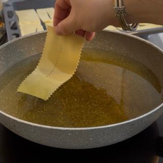 Una persona tiene in mano un pezzo di pasta sopra una padella piena d'olio.