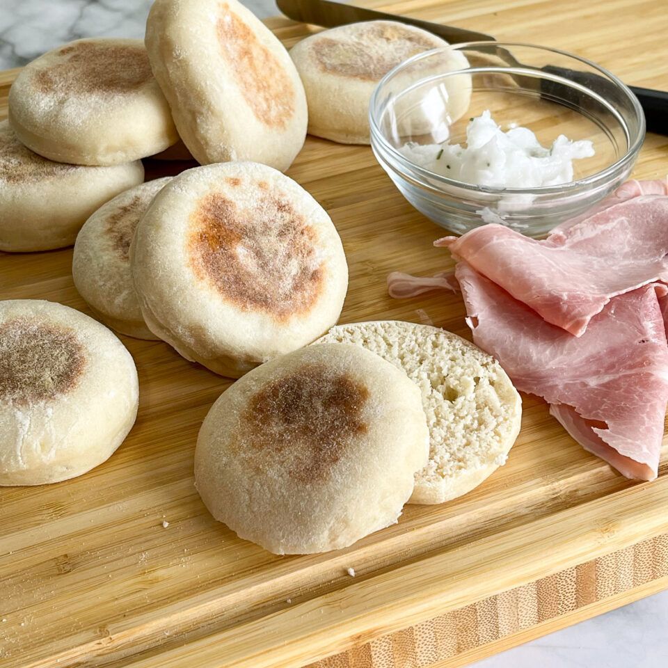 Un tagliere di legno con sopra muffin inglesi e prosciutto.