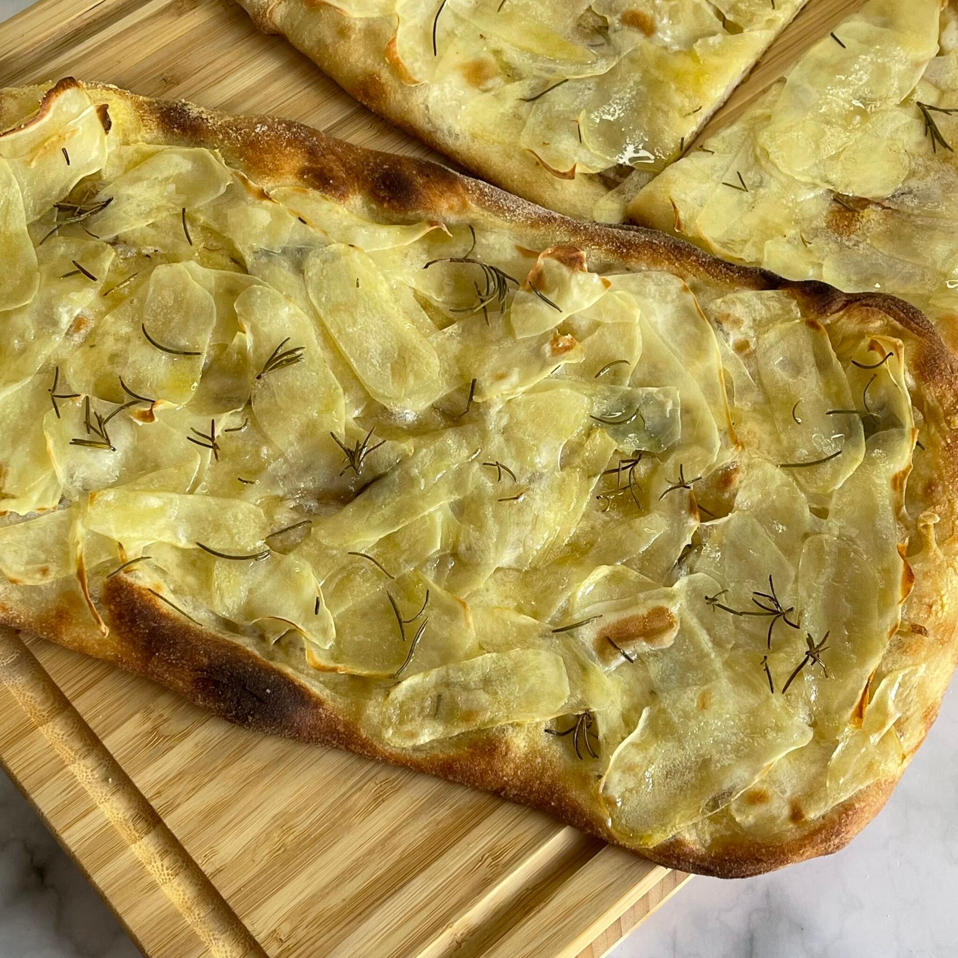 Una pizza con patate e formaggio su un tagliere di legno.