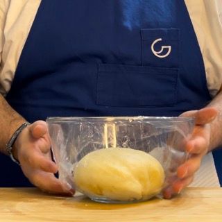 Un uomo con un grembiule tiene in mano una ciotola di pasta