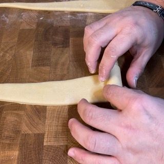 Una persona sta tagliando un pezzo di pasta su un tagliere di legno.