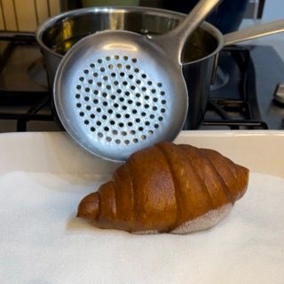 Un croissant è appoggiato su un tovagliolo di carta accanto a un mestolo