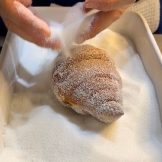 Una persona sta mettendo dello zucchero a velo su una ciambella in una padella.