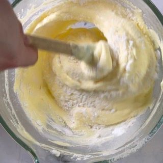 Una persona sta mescolando un impasto in una ciotola di vetro con un cucchiaio di legno.