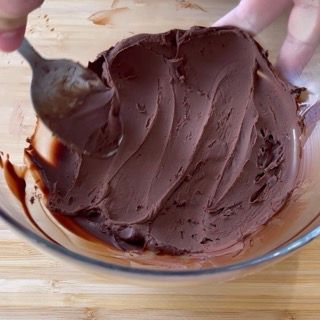 Una persona sta mescolando una ciotola di glassa al cioccolato con un cucchiaio