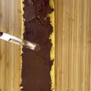 Una persona sta spalmando la glassa al cioccolato su una fetta di torta su un tagliere di legno.