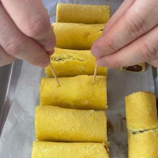 Una persona infila degli stuzzicadenti in una fila di panini gialli