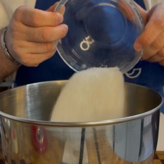 Una persona sta versando lo zucchero in una ciotola di metallo