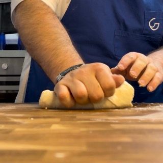 Un uomo con un grembiule blu sta impastando la pasta su un tagliere