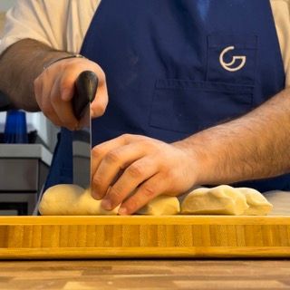 Un uomo con un grembiule blu sta tagliando il pane su un tagliere
