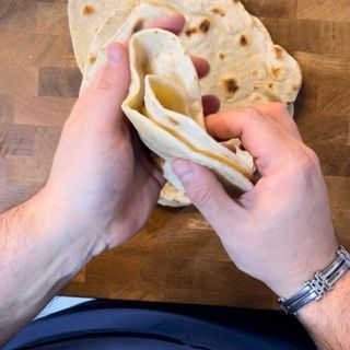 Una persona che indossa un orologio tiene una tortilla tra le mani