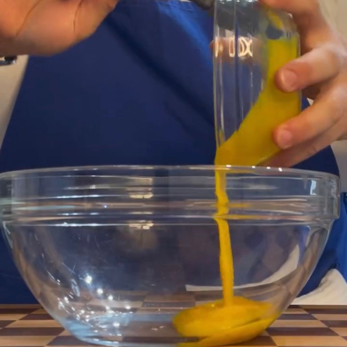 Una persona che versa del liquido giallo in una ciotola di vetro