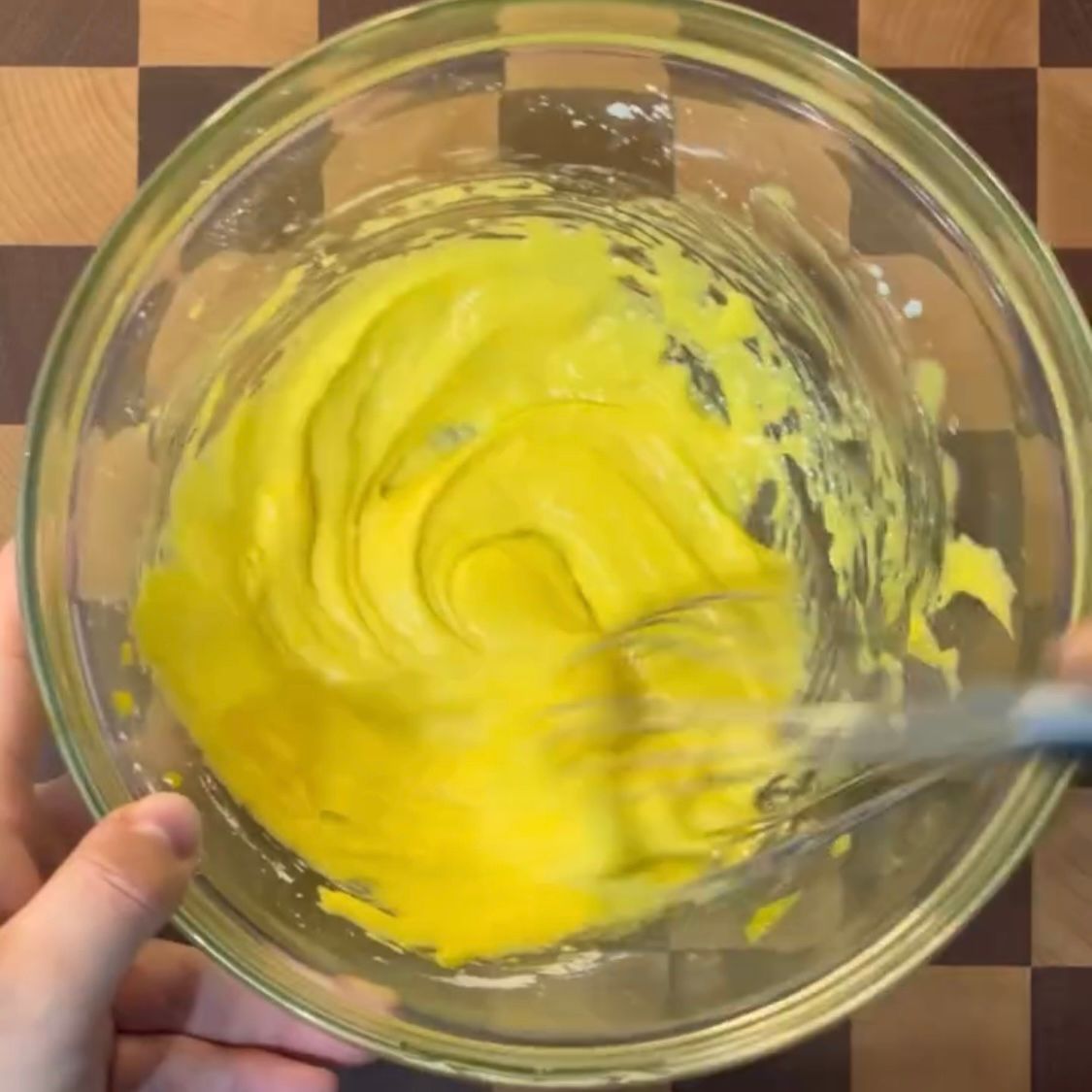 Una persona sta sbattendo un liquido giallo in una ciotola di vetro
